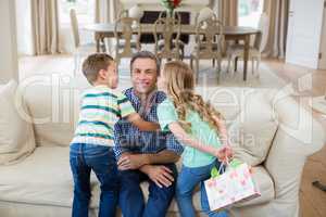 Son and daughter kissing their father on cheek in living room