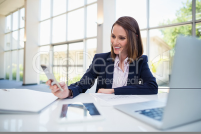 Businesswoman sitting at desk and using mobile phone