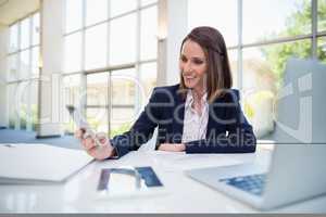 Businesswoman sitting at desk and using mobile phone