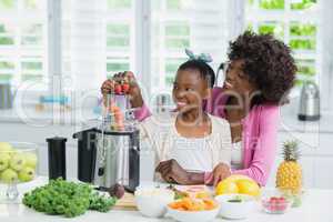 Smiling mother and daughter preparing strawberry smoothie in kitchen