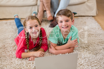 Sibling lying on rug with laptop in living room