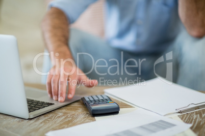 Man using laptop with bills on table in living room