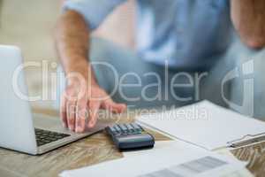 Man using laptop with bills on table in living room