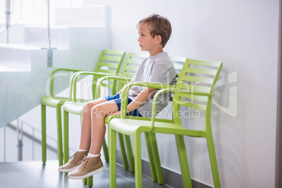 Upset boy sitting on chair in corridor