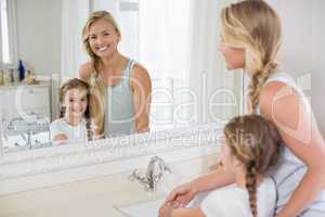 Happy mother and daughter washing hands in bathroom sink