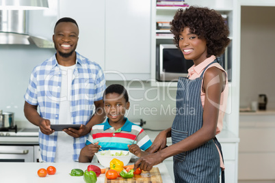 Mother and son preparing salad while father using digital tablet in kitchen at home