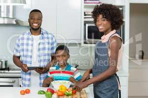 Mother and son preparing salad while father using digital tablet in kitchen at home