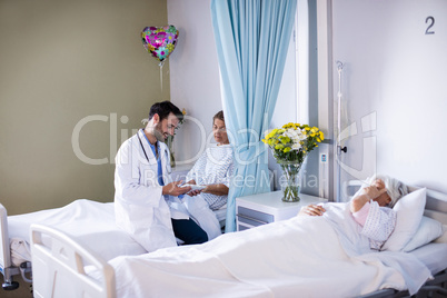 Male doctor interacting with female senior patient in the ward