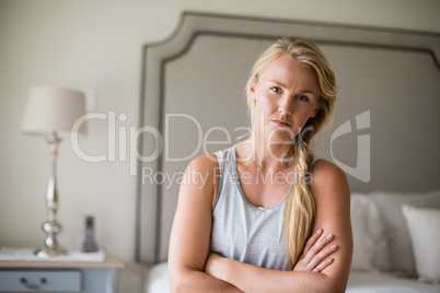 Beautiful woman sitting on bed with arms crossed in bedroom