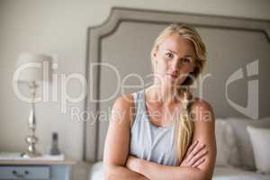 Beautiful woman sitting on bed with arms crossed in bedroom