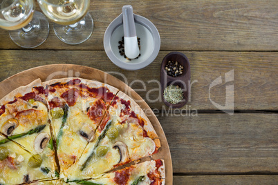 Italian pizza served in a pizza tray with wine glasses and ingredients on a wooden plank