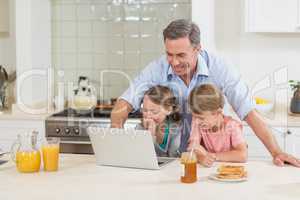 Father and his kids using laptop while having breakfast