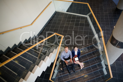 Businessman and woman sitting on steps using laptop and digital tablet