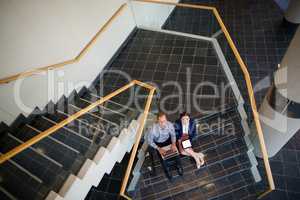 Businessman and woman sitting on steps using laptop and digital tablet