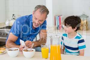 Father showing mobile phone to son while having breakfast