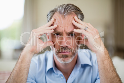 Tense man with hand on forehead sitting on sofa in living room