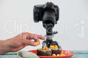 Photographer keeping yellow cherry on dessert, camera in background