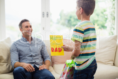 Son giving birthday card to father in living room