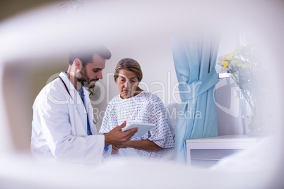 Male doctor showing digital tablet to female senior patient in the ward