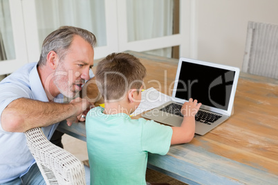 Father assisting son while using laptop at desk