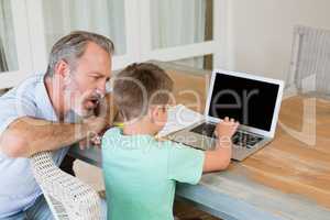Father assisting son while using laptop at desk