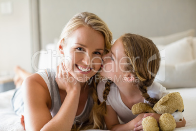 Daughter kissing her mother on cheek in bedroom