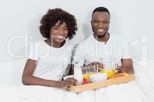 Portrait of smiling couple having breakfast in bedroom