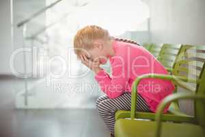 Upset girl sitting on chair in corridor