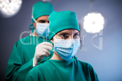 Surgeon helping a nurse in tying surgical mask in operation room