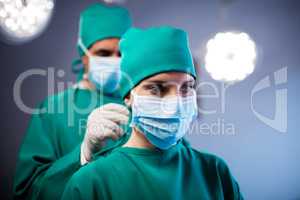 Surgeon helping a nurse in tying surgical mask in operation room