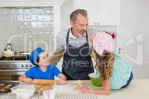 Father and kids having fun while making dough in kitchen