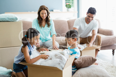 Parents and kids unpacking carton boxes in living room