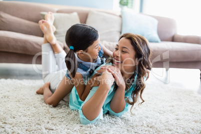 Happy daughter and mother interacting with each other while lying on rug