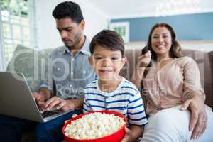 Portrait of boy with mother watching television and father using laptop in background