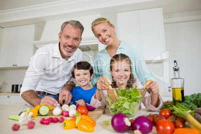 Smiling parents and children preparing vegetable salad in kitchen