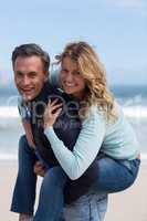 Mature man giving piggyback ride to woman on beach