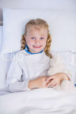Sick girl with teddy bear in hospital bed