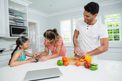 Mother and daughter using digital tablet and father watching her in kitchen