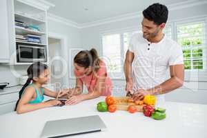 Mother and daughter using digital tablet and father watching her in kitchen