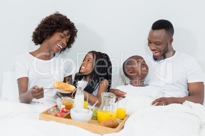 Smiling parents and kids having breakfast in bedroom