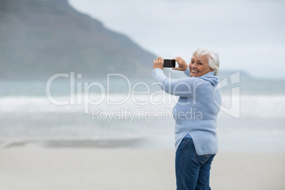 Senior woman photographing scenery using cell phone on the beach