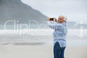 Senior woman photographing scenery using cell phone on the beach