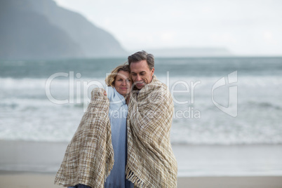 Mature couple wrapped in blanket on the beach