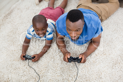 Father and son lying on rug and playing video game
