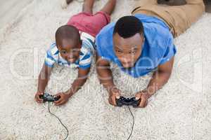 Father and son lying on rug and playing video game