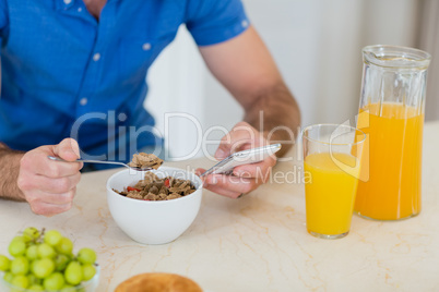 Man using mobile phone while having breakfast in kitchen