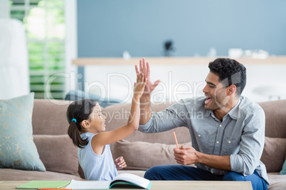 Father giving high five to daughter while helping her in homework