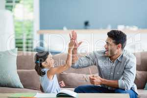 Father giving high five to daughter while helping her in homework