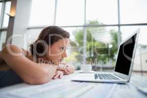 Businesswoman leaning on desk and looking at laptop