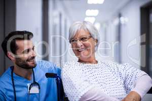 Male doctor interacting with senior patient on wheel chair in the corridor